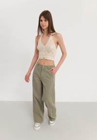 Svijetlo bež heklani halter top s teksturiranim uzorkom i akcentima s gumbima, uparen s labavim maslinasto zelenim cargo hlačama.