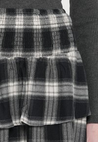 Black and white plaid fabric with layered ruffles; textured with elastic waistband; features contrasting thin white stitch lines.