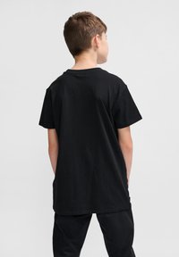 Tricou negru din bumbac, cu mâneci scurte și decolteu rotund. Prezintă o croială lejeră, o culoare uniformă și o textură netedă.