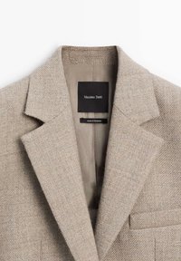 Beige wollen blazer met gekartelde kraag, enkele borstzak en subtiele textuur. Voering zichtbaar met merklabel.