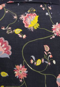 Tejido azul marino con un patrón floral que presenta flores en rosa, amarillo y verde. Pequeño detalle de logo metálico en la parte superior. Textura suave.