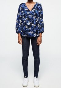 Námořnická květinová blůza s dlouhými rukávy, která má volný výstřih a bílé květinové vzory, spárována s tmavými úzkými džíny a bílými teniskami.