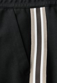 Tissu noir avec des rayures verticales beige, gris foncé et blanc à côté d'une couture et d'un détail de coutures froncées.