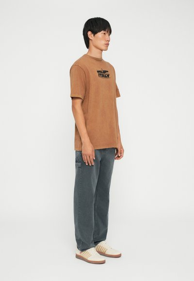 Brun bomull t-skjorte med en svart "ITALY" grafikk på brystet, parret med grå cargo-bukser og kremhvite sneakers med brune striper.