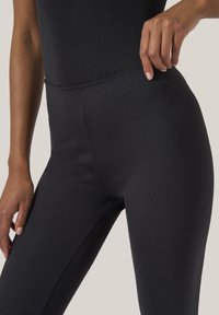 Svarta leggings gjorda av elastiskt material, med en åtsittande design och slät textur, samt en hög midja för komfort och stöd.