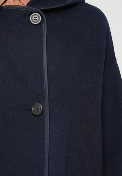Palton dintr-un amestec de lână de culoare bleumarin, cu glugă, având o textură netedă, închidere cu nasturi în partea din față și margini cu detalii contrastante.