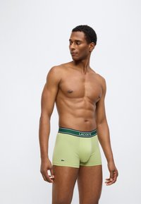 Πράσινα βαμβακερά μποξεράκια με μαύρη και λευκή ελαστική μέση που φέρει το λογότυπο "Lacoste" στο μπροστινό μέρος. Λείο, εφαρμοστό σχέδιο.