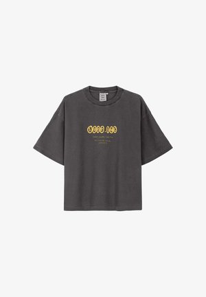 Ciemnoszary oversize t-shirt z krótkim rękawem z żółtą grafiką tekstową "SURF. INC" i mniejszym tekstem poniżej na środku przodu.