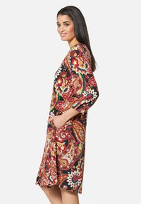 Bunt bedrucktes Paisley-Kleid mit Dreiviertelärmeln, seitlichen Taschen, knielangem Saum und schwarzem Hintergrund mit roten, gelben und grünen Akzenten.