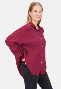 Burgunderfarbenes Hemd mit Knöpfen aus strukturiertem Stoff, mit einem Kragen und lockerer Passform, kombiniert mit schwarzen Hosen.