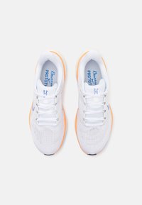 White athletic shoes with mesh upper, orange accents on sole, flat laces, and blue branding on insole. Rounded toe and textured surface.