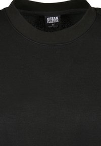 T-shirt noir à col rond avec une étiquette "Urban Classics XS Fabriqué en Chine" visible à l'intérieur du col.