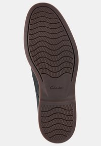 Semelle d'une chaussure Clarks noire avec un motif de semelle en vagues et en diamants pour une meilleure adhérence, et le nom de la marque estampé au centre de la voûte.