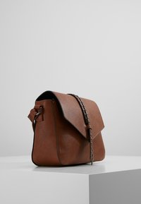 Brązowa skórzana torebka na ramię z klapką, srebrnymi elementami i ozdobnymi ćwiekami na pasku. Gładka faktura, prostokątny kształt.