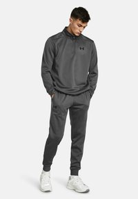 Sudadera deportiva gris con media cremallera y pantalones ajustados. Presenta una textura suave y acentos de logo en negro.