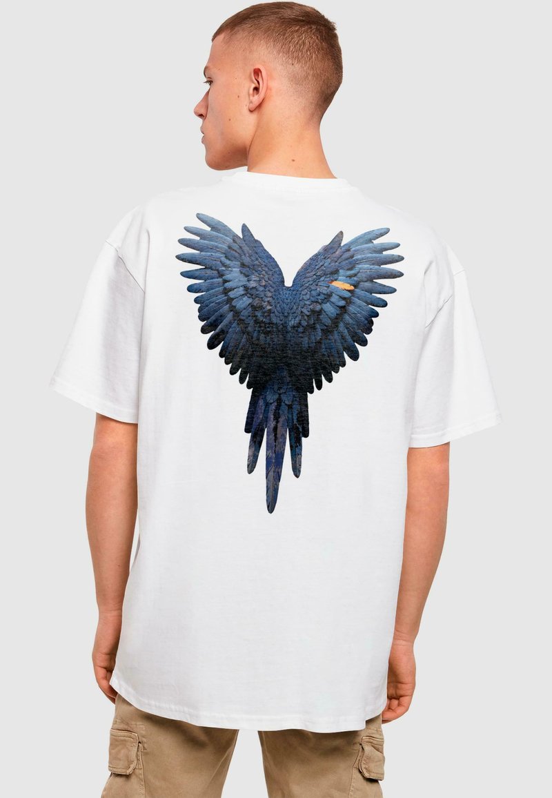 White oversized t-shirt featuring a blue wing design printed on the back, showcasing detailed feather textures and a graphic style.