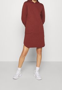 Czarna sukienka z kapturem wykonana z burgundowej tkaniny, z długimi rękawami, z dwoma przednimi kieszeniami i zaokrąglonym dołem. Połączona z białymi sneakersami i skarpetkami.