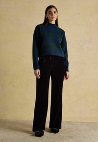 Roheline ja tumesinine argyle mustriga sviiter kõrge kaelusega, kombineeritud mustade sametist laiade pükste ja mustade rõhutatult lipsukesega kingadega. Lihtne ehe.