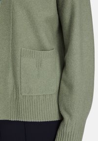 Grüner gestrickter Cardigan mit strukturierter Oberfläche, geripptem Saum und Bündchen sowie einer Vordertasche. Das Material wirkt weich und warm.