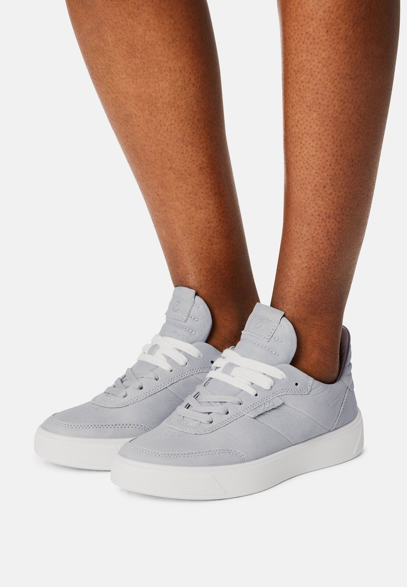 Sneaker in pelle grigia con lacci bianchi e suole in gomma. Presentano una texture sottile e un tassello sul tallone rinforzato.