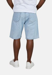 Cortos de denim azul claro con un ajuste relajado, que cuentan con bolsillos traseros y bordes doblados, combinados con zapatillas blancas.