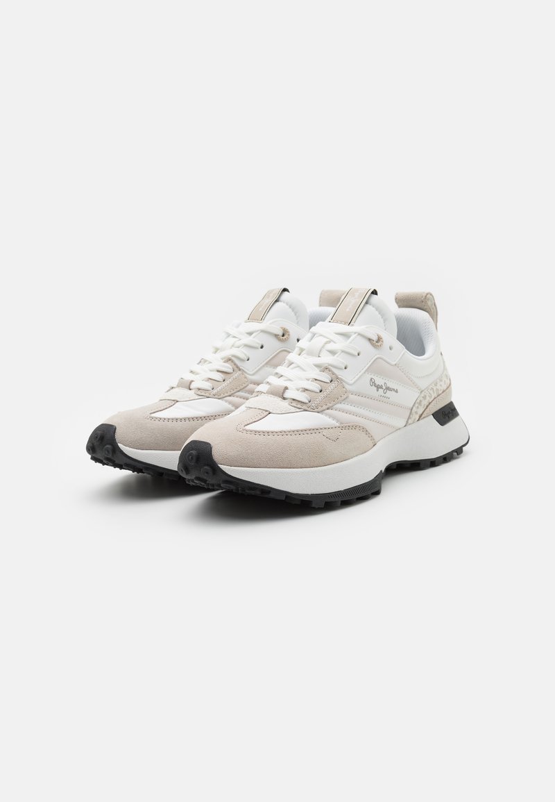 Sneakers beige chiaro con tomaia in rete e camoscio, lacci bianchi, suola in gomma nera e dettagli metallici sul tallone e sulla linguetta.