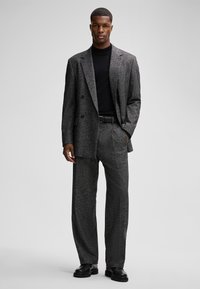 Grijze getailleerde pak met een dubbel-gebouwde blazer en brede broek, gecombineerd met een zwarte coltrui en zwarte schoenen. Glad textuur.