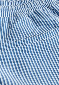Tissu léger à rayures verticales bleu et blanc avec couture visible et texture subtile, suggérant un détail de vêtement.