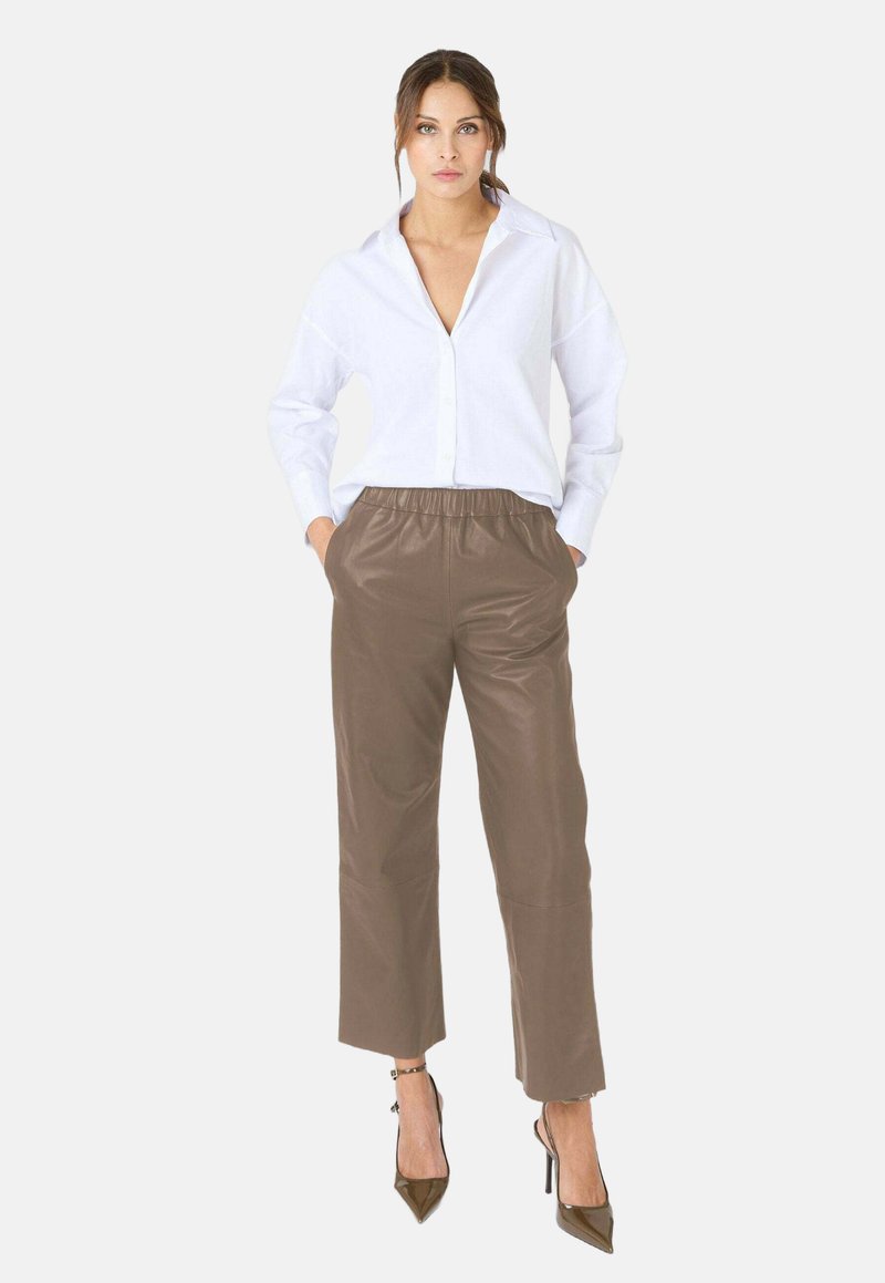 Witte overhem shirt met een kraag, gecombineerd met bruine leren broeken met een elastische tailleband en een relaxte pasvorm. Het model draagt enkellaarsjes met straps.