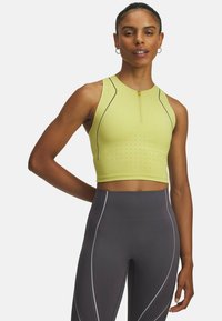 Svetlozelený športový crop top na zips s perforovanými detailmi a kontrastnými švami, v kombinácii s tmavošedými legínami s vysokým pásom a bielymi akcentmi.
