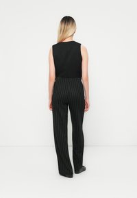 Haut sans manches noir associé à un pantalon large à rayures noires, tissu lisse, avec des fentes sur les côtés. Des chaussures noires complètent la tenue.