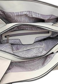 Intérieur d'un sac en cuir blanc avec compartiment zippé. Doublé de tissu violet clair comportant un texte répétitif et le logo "SURI FREY."
