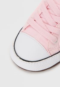 Jasnoróżowe płócienne trampki z białą gumową czubkiem, czarnym wykończeniem i teksturowanymi sznurówkami. Zbliżenie ukazujące detale szwów i materiału.