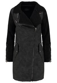 Cappotto in finta pelle scamosciata nera con colletto in pelliccia shearling morbida, cerniera asimmetrica e due tasche frontali con chiusura a zip. Tessuto liscio e design di lunghezza media.