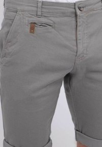 Shorts gris en tissu texturé, avec fermeture à bouton et zip, poches avant, et ourlet retroussé avec une étiquette de marque discrète.