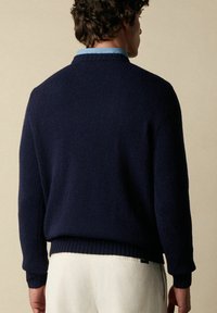Maglione a maglia blu navy con orlo e polsini a coste, indossato sopra una camicia colletto azzurro, che mette in mostra un tessuto morbido e texture.