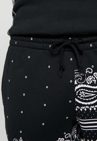 Černé tepláky s bílými puntíky a vzorem paisley. Obsahují šňůrku v pase a žebrovanou texturu pro pohodlí.