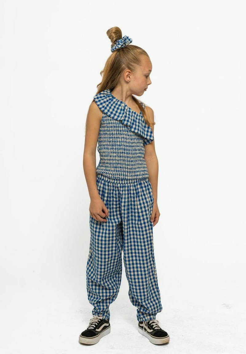 Kék és fehér kockás öltözet, egy vállas, fodros felsővel, smockolt melltartóval és laza szabású kockás nadrággal. Tartalmaz egy illeszkedő hajgumit is.