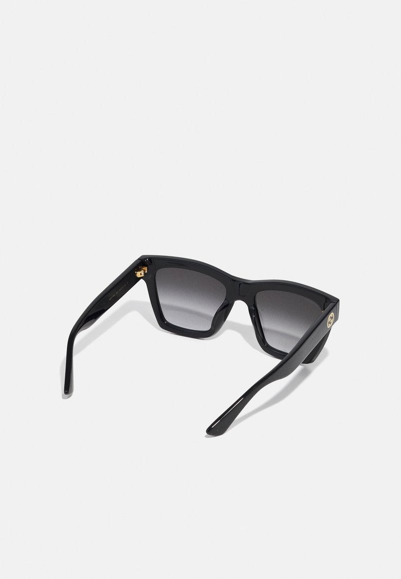 Lunettes de soleil noires avec une monture carrée, verres gris dégradés, matériau plastique brillant et accent doré sur la branche.