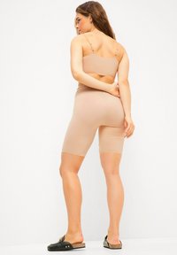 Beige sportoutfit bestaande uit een goed aansluitende bralette en shorts tot halverwege de dijen, gemaakt van een gladde, elastische stof. Minimalistisch ontwerp met verstelbare bandjes.