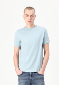 Ανοιχτό μπλε βαμβακερό T-shirt με στρογγυλή λαιμόκοψη και κοντά μανίκια, διαθέτει ένα μικρό λογότυπο στην αριστερή πλευρά του στήθους. Λείος υφασμάτινος χαρακτήρας, άνετη εφαρμογή.