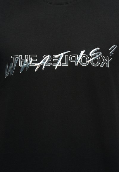 Μαύρο ύφασμα με επικαλυπτόμενο κείμενο: λευκά περιγραμμικά γράμματα «THE KOOPLES?» και ασημί ανακλαστικά γράμματα «WHAT IS?» στο κέντρο.