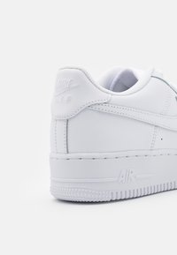 Bílé kožené tenisky mají polstrovaný límec, embosované logo "Nike AIR" na zadní straně a texturovanou gumovou podrážku s detaily hvězdiček.