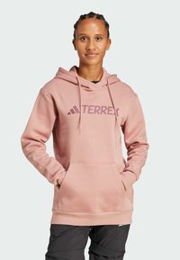 Hoodie rosa chiaro con tasca frontale e cappuccio con coulisse, con il logo "TERREX" stampato in rosa scuro sul petto. Tessuto in una consistenza solida.