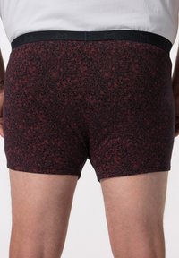 Boxer da uomo a fantasia nera e rossa con un design floreale, dotati di una cintura liscia con la lettera "M" impressa.