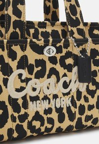 Sac fourre-tout en imprimé léopard avec une toile beige et noire, garnitures en argent, et logo "Coach New York" brodé. Inclut une étiquette noire.