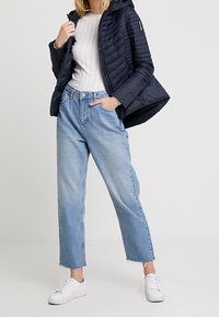 Chaqueta acolchada de marina con capucha, diseño ligero y acolchado; parte superior gris de canalé; vaqueros de pierna recta de lavado claro con dobladillo deshilachado; zapatillas blancas.