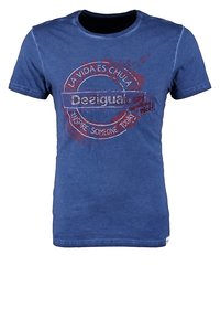 Niebieska bawełniana koszulka z okrągłym dekoltem. Posiada grafikę z tekstem w kolorze czerwonym i białym: "Deeigual," "La vida es chula," oraz "Inspire someone today."