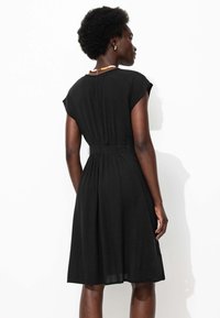 Robe noire avec des manches courtes en forme de cap, taille ajustée, jupe évasée, fabriquée à partir d'un tissu léger. Elle présente une texture lisse et un design simple.