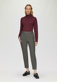 Bordeauxfarbener Rollkragenpullover kombiniert mit maßgeschneiderten grauen Anzughosen. Die Hosen besitzen eine glatte Textur und eine leicht verkürzte Beinin passform. Schwarze Schuhe runden das Outfit ab.